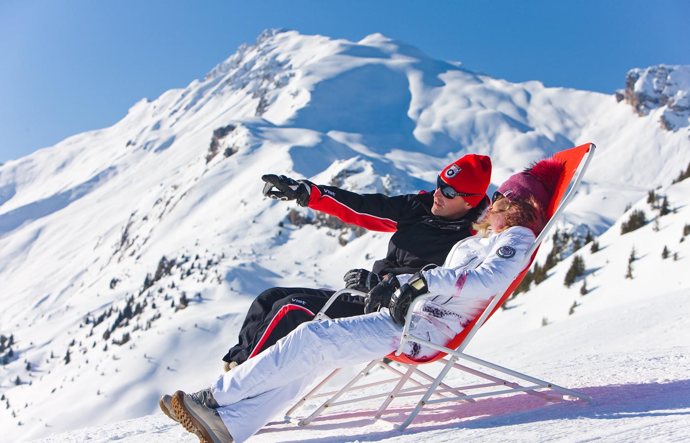 Pärchen auf einem Sonnenstuhl in schneebedeckter Landschaft auf dem Berg